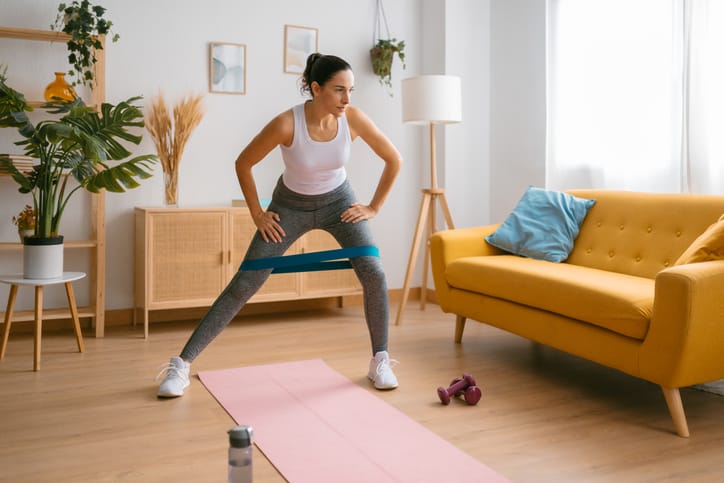 Photo shows a woman using an elastic band to exercise at home/Getty Images