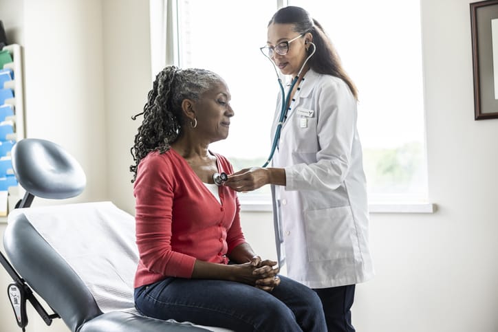 Photo shows a female doctor listening to senior woman's heart in an exam room/Getty Images