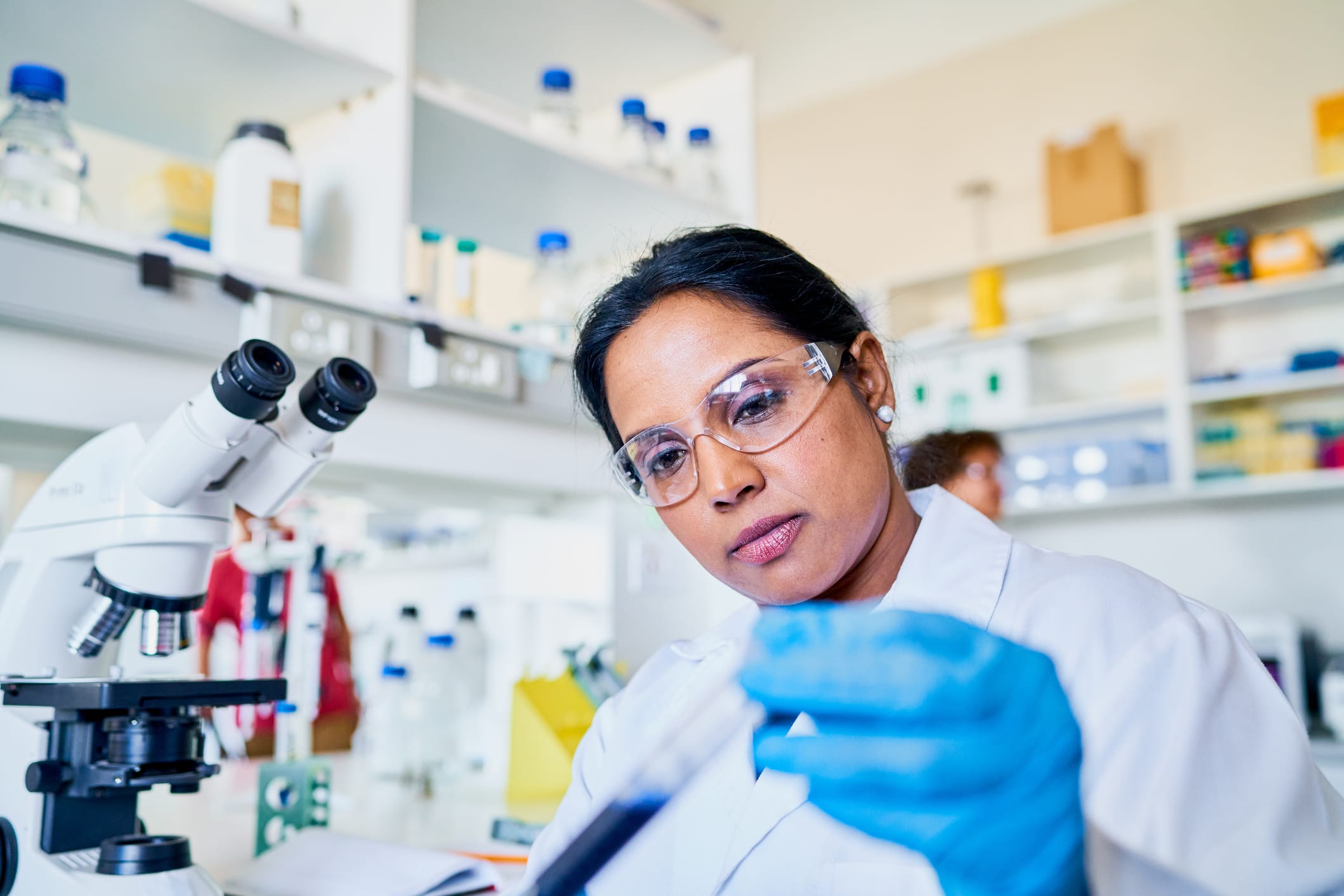 Female scientist examining a sample in a text tube while working by a microscope in a lab