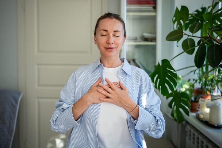 Woman with hands held to chest and eyes closed