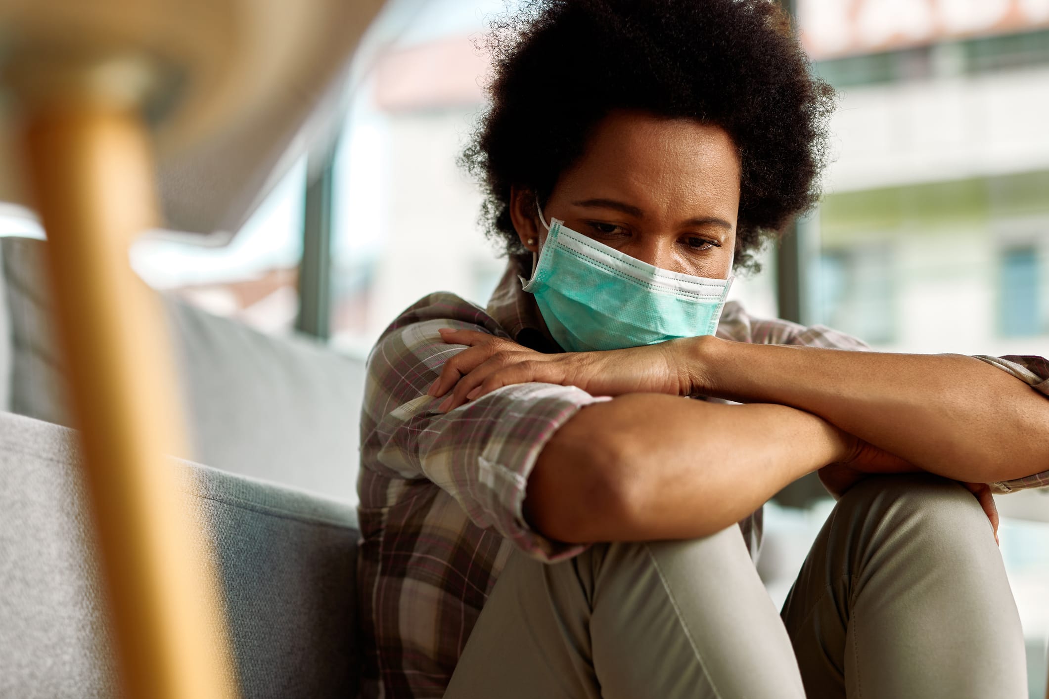 Sad African American woman wearing face mask while sitting at home