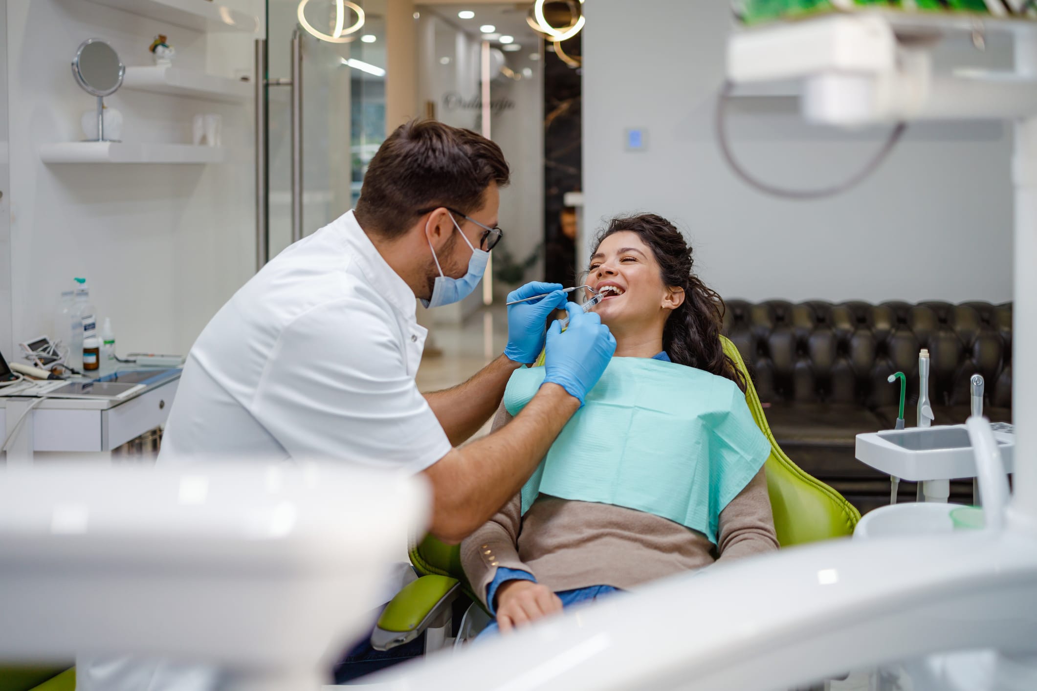 A dentist in protective gear is checking a female patient’s teeth