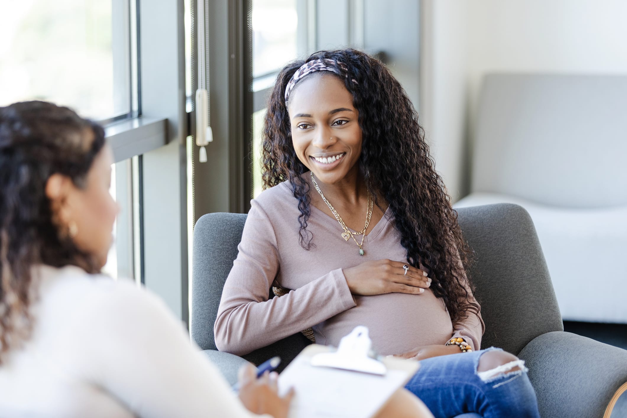 The expectant young adult woman smiles as she listens to advice from her unrecognizable female counselor.