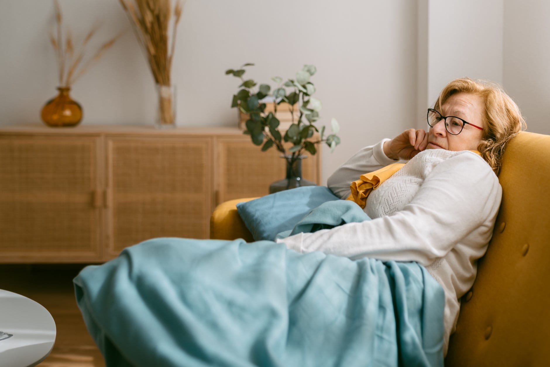 Tired-looking women sitting alone on couch under blanket