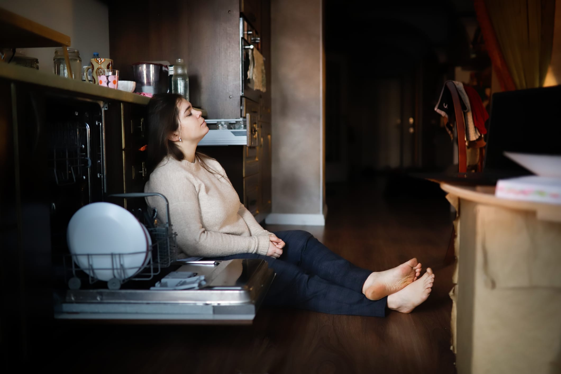 Tired woman sitting on floor next to dishwasher