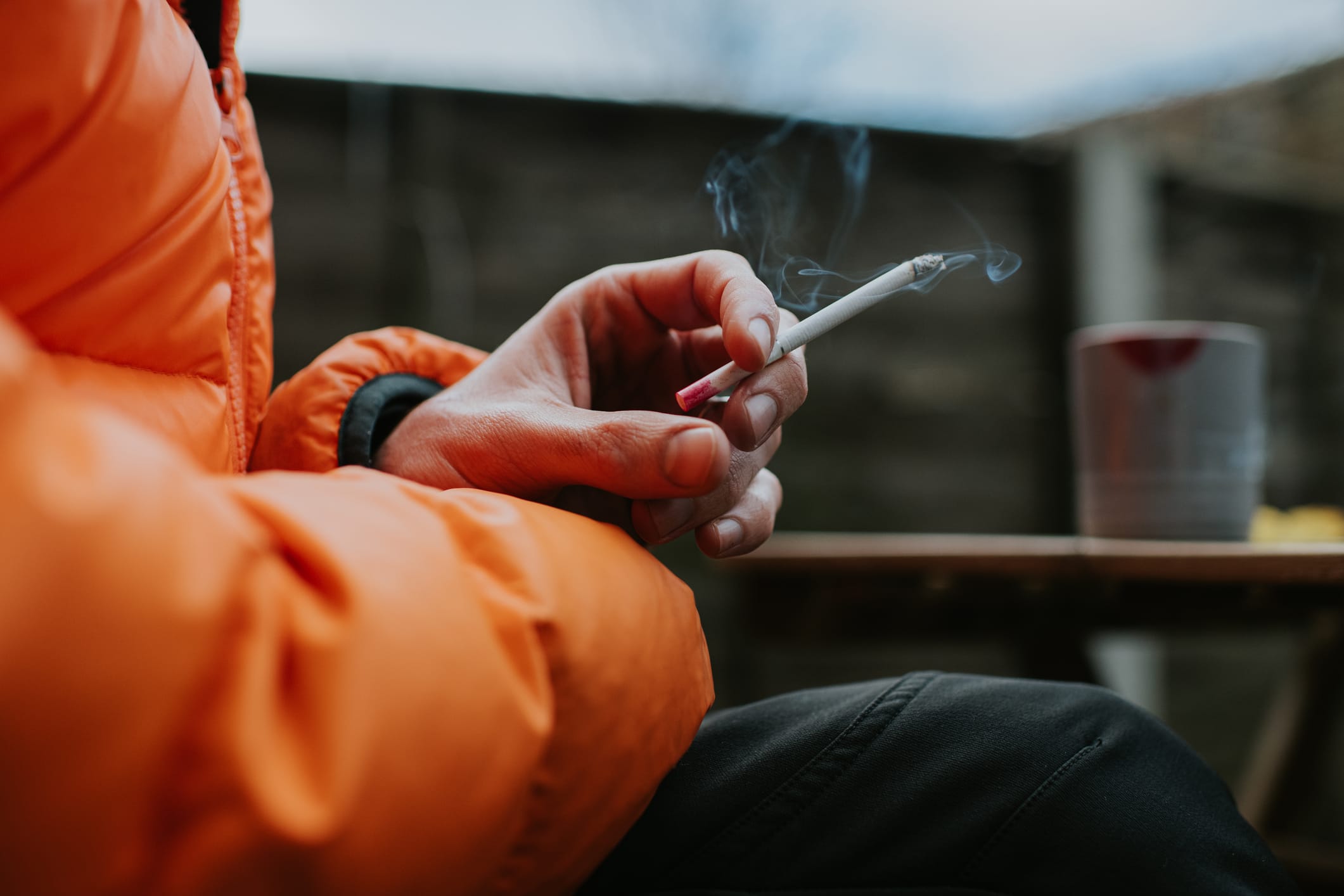 A man sits outside and holds a slim menthol cigarette between his fingers.