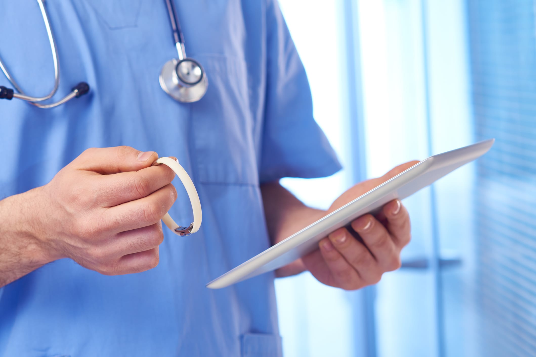 Doctor using tablet computer and holding medical ID bracelet